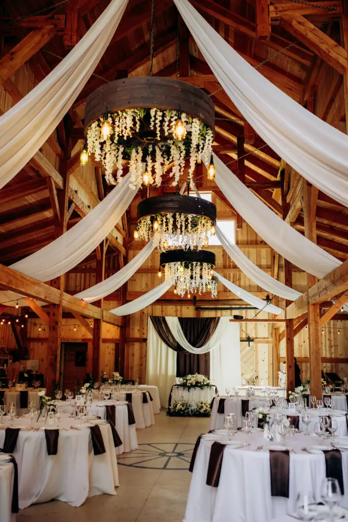 Timber-frame barn wedding reception setup at Barn Owl Venue with decorated tables, draped beams, and warm natural lighting.